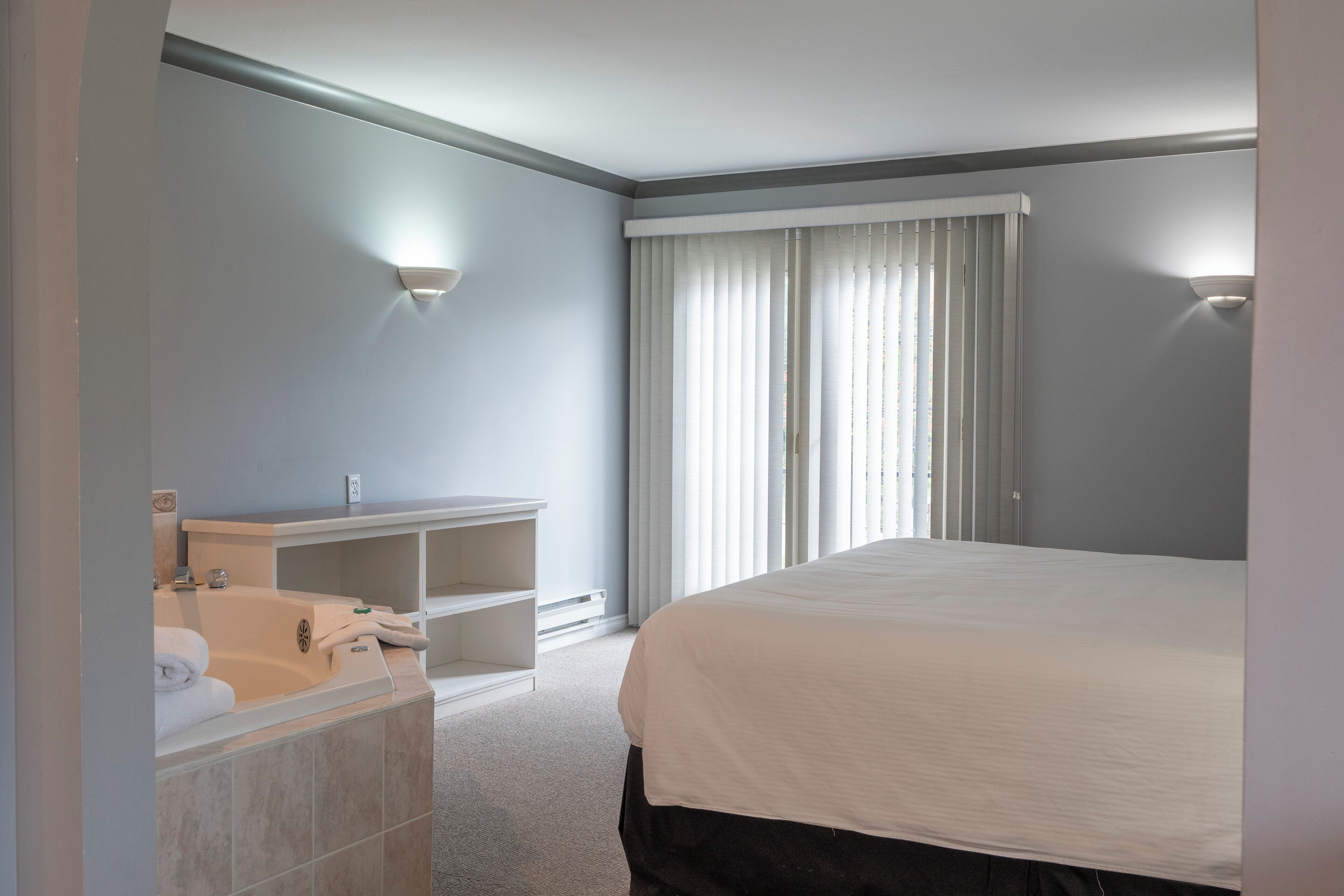 Camera d'albergo con un letto grande, una vasca da bagno, un comò con uno specchio e due luci a parete.