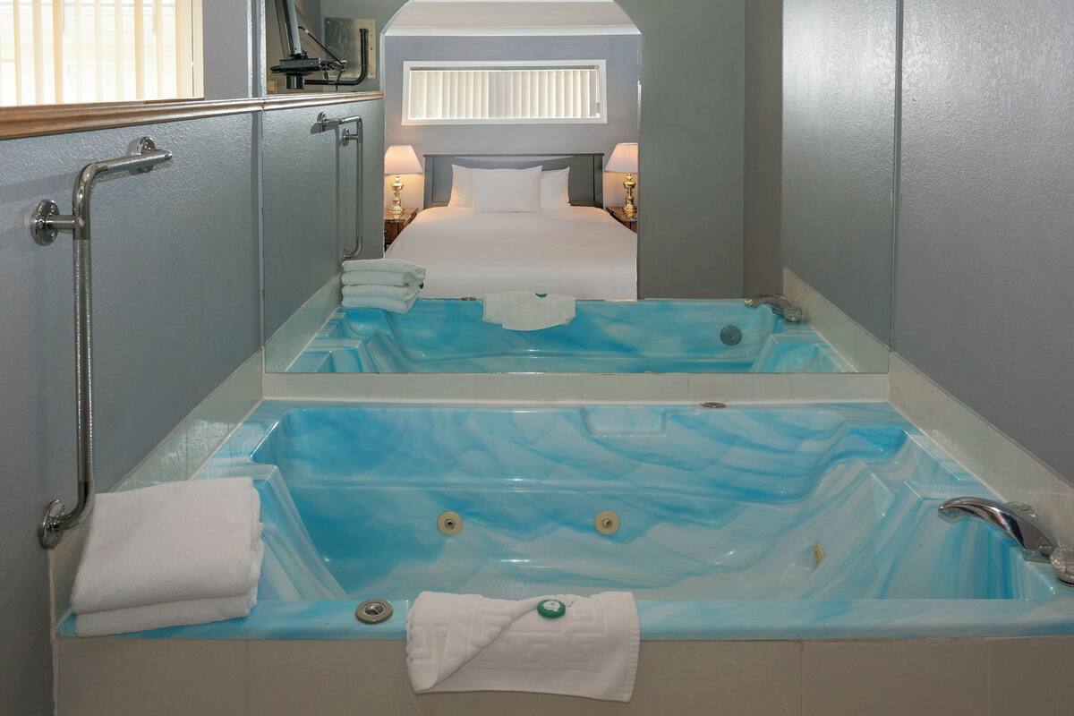 A bathroom with a large bathtub, a shower, and a toilet. There are towels and toiletries on the floor.