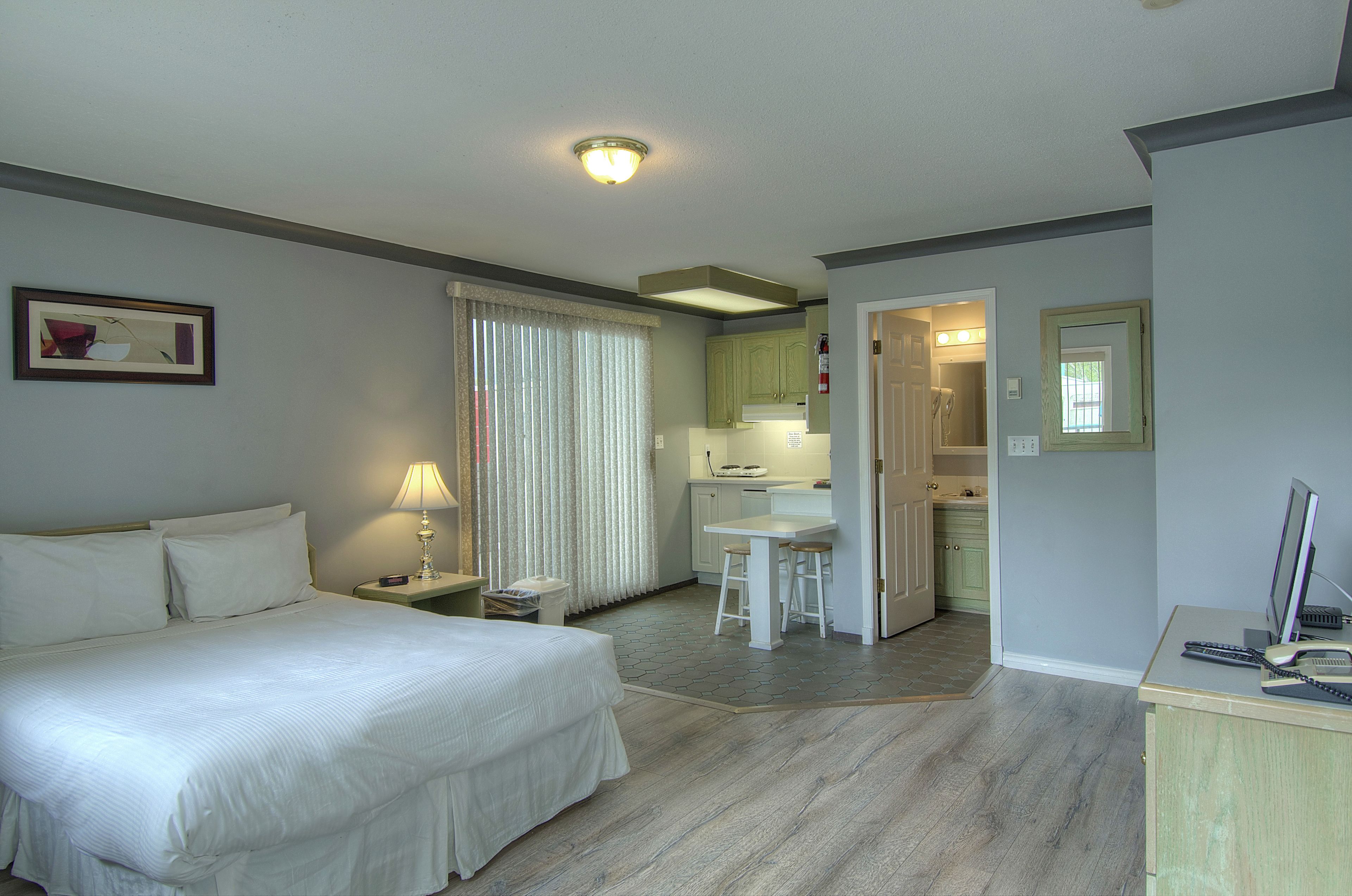 Een hotelkamer met een bed, een bureau, een stoel, een computer en een kitchenette.