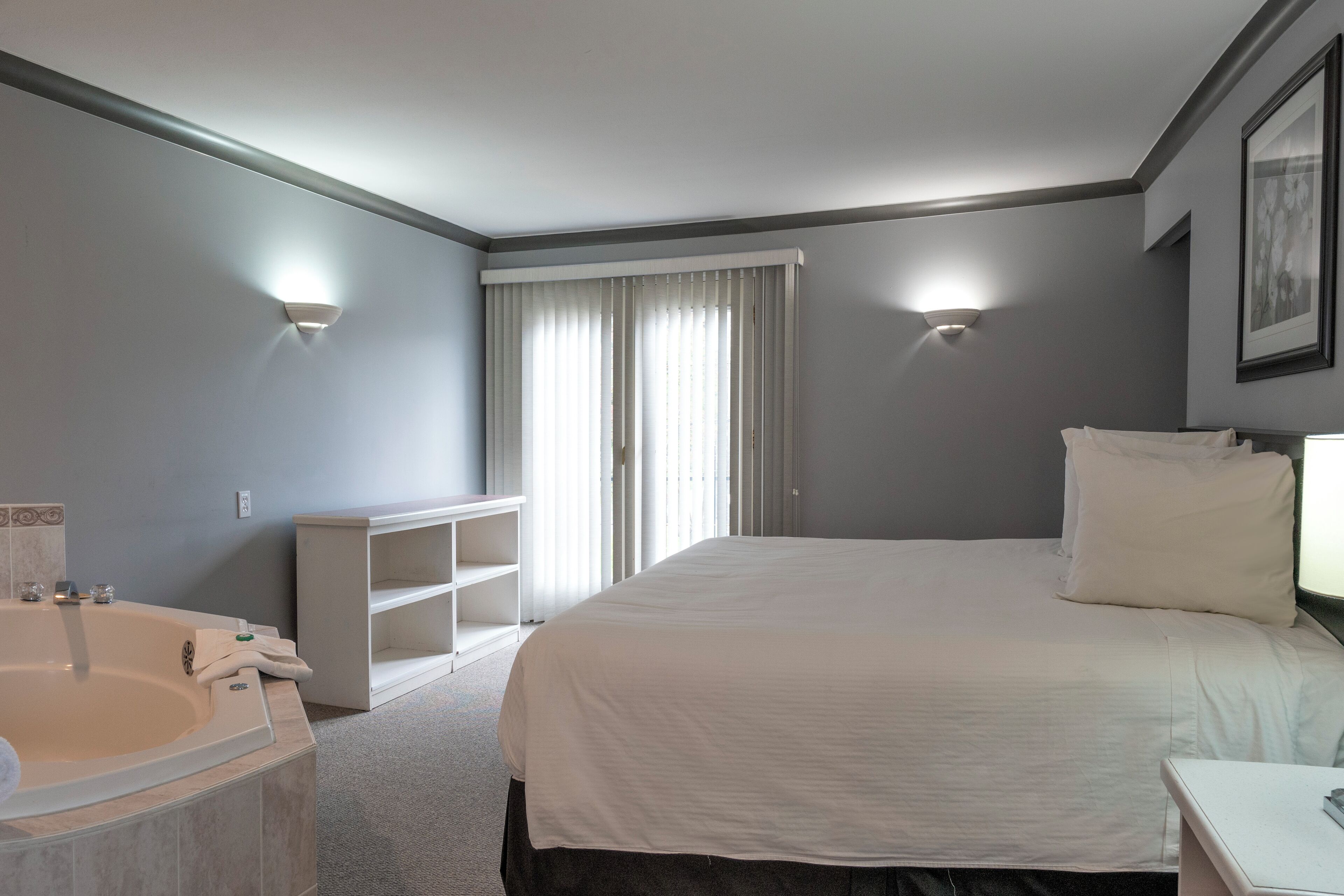 A hotel room with a large bed, a separate bathroom with a bathtub, and a small table.
