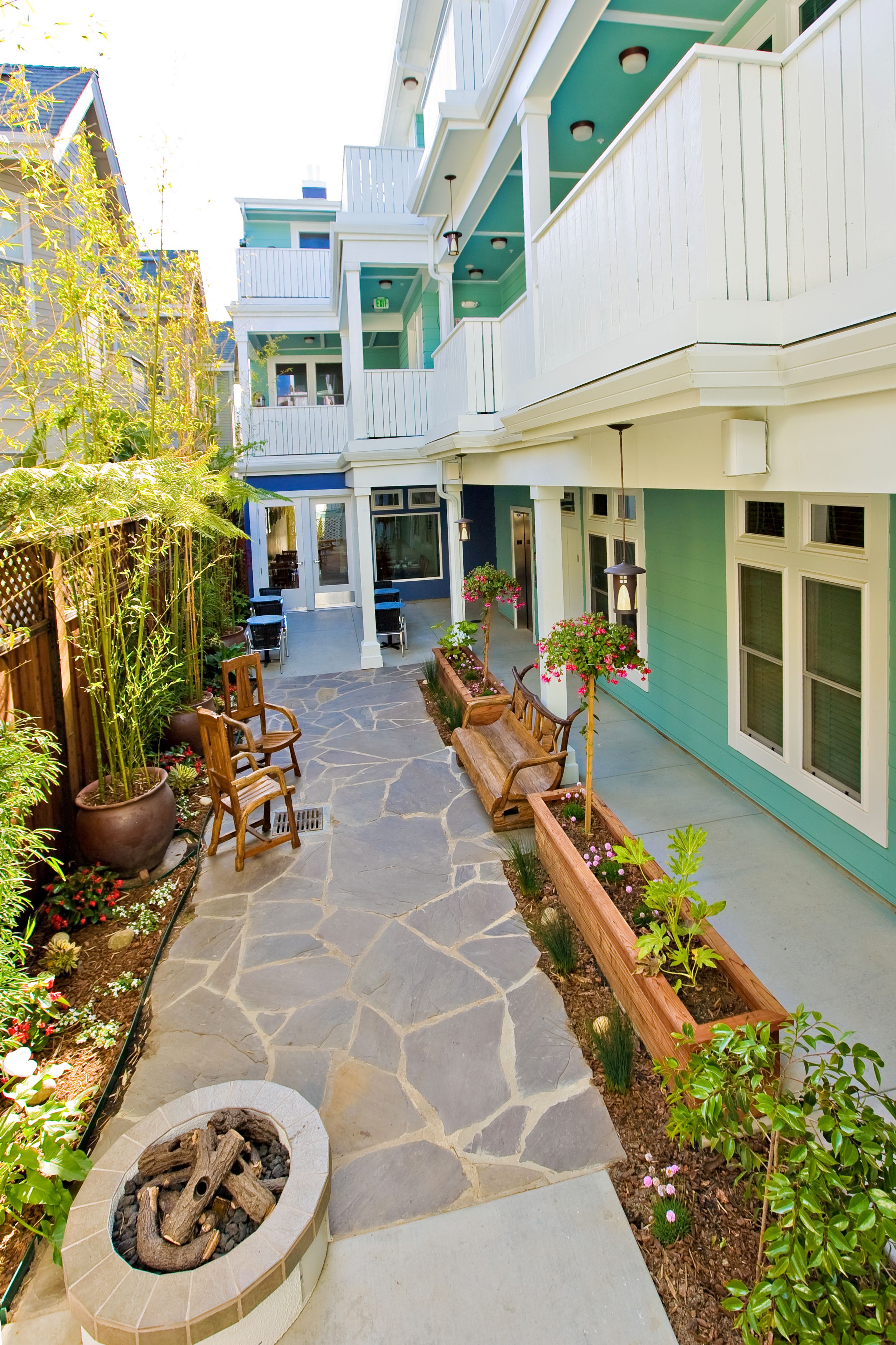 A courtyard with stone flooring, wooden benches, and potted plants.
