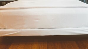 Una cama bien tendida en una habitación con paredes azul claro, suelo de madera y dos mesitas de noche con lámparas.