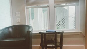 Una habitación con piso de madera, un sillón de cuero negro, una mesita con una computadora portátil y una ventana con persianas.