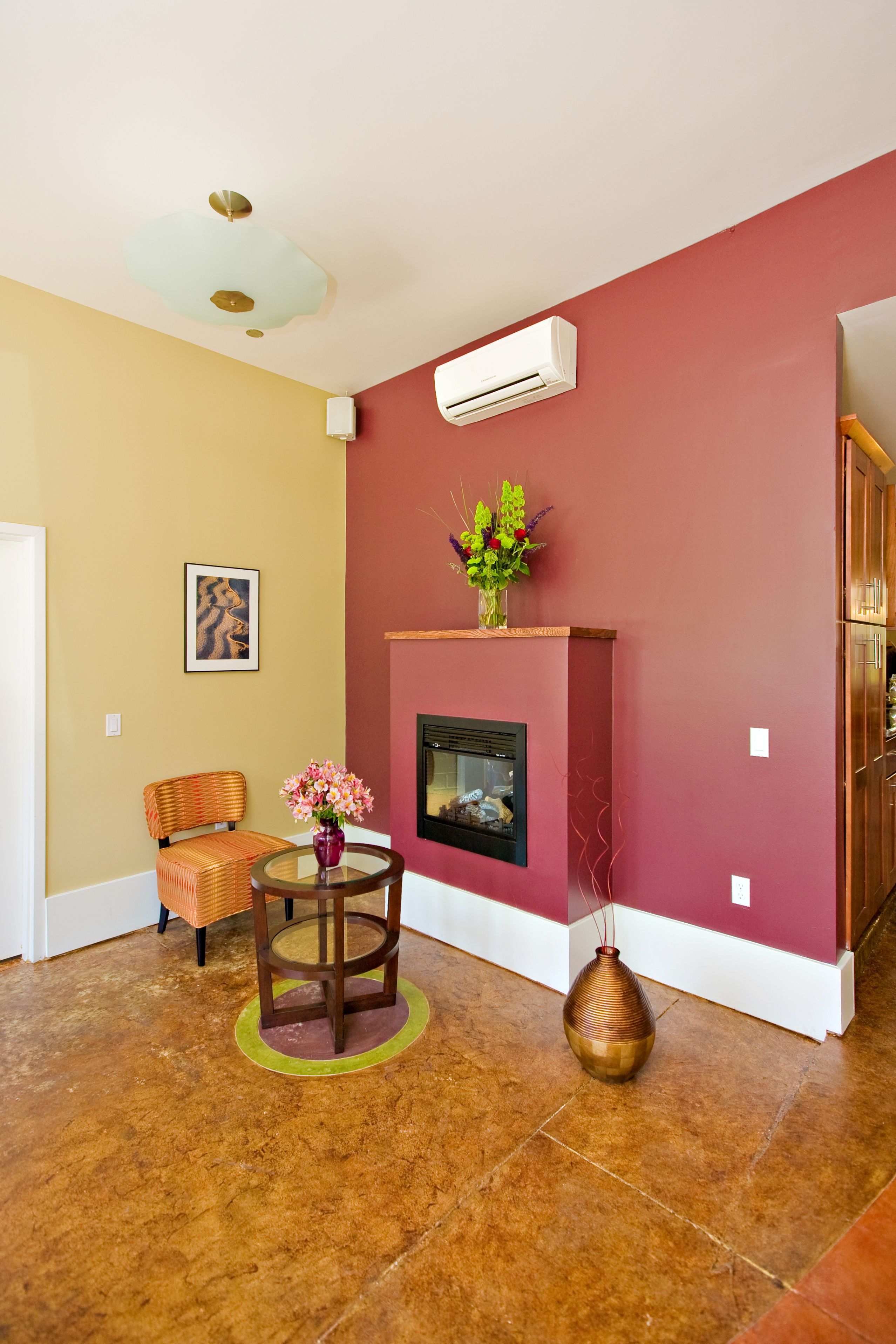 A living room with a fireplace, a chair, a small table with flowers, and a vase.
