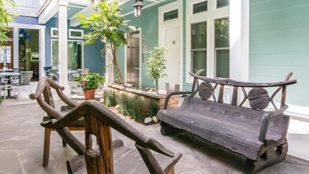Un banco de madera y una mesita en un patio con plantas en macetas y un edificio al fondo.