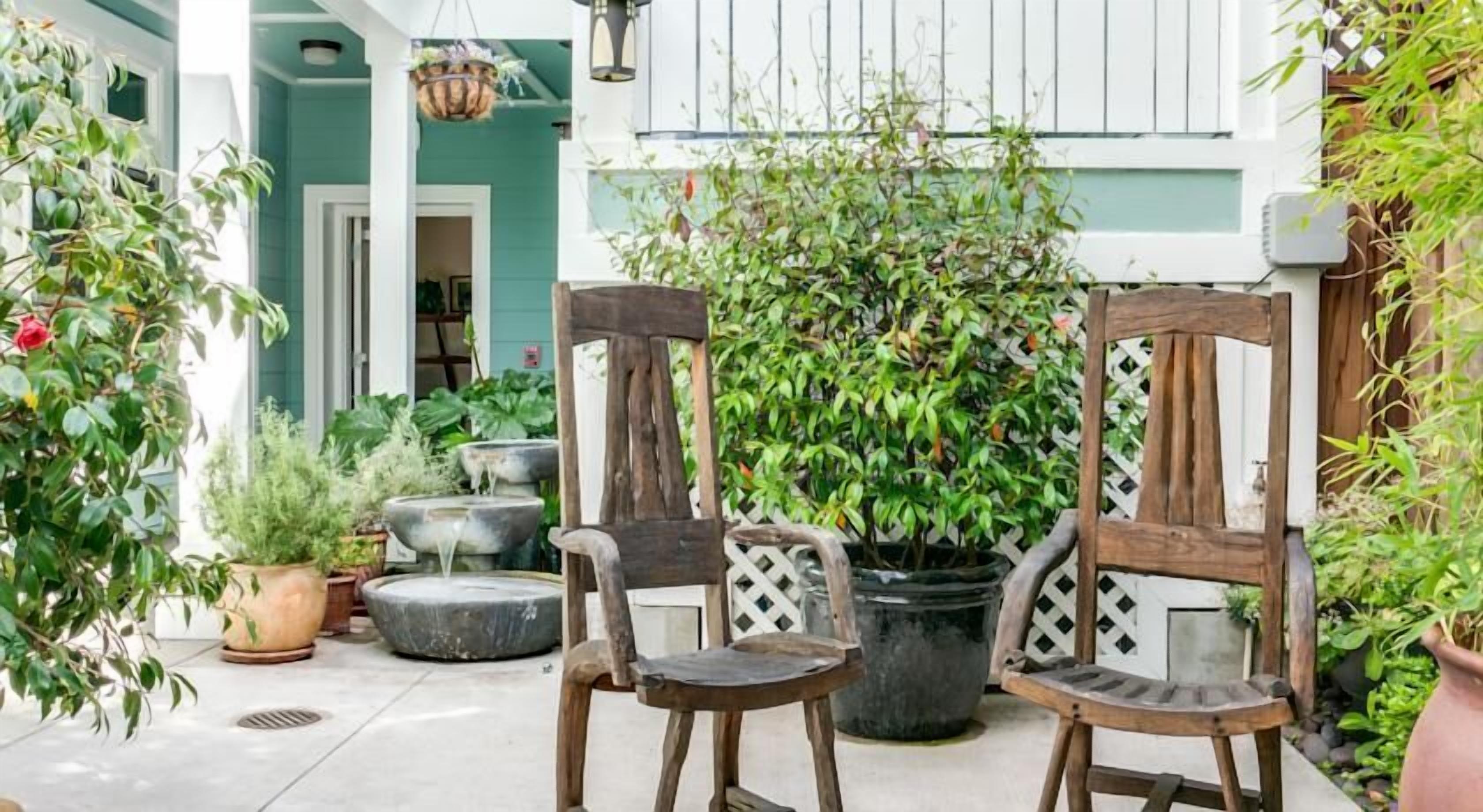 Un patio con dos sillas de madera, una fuente de piedra y varias macetas con plantas.