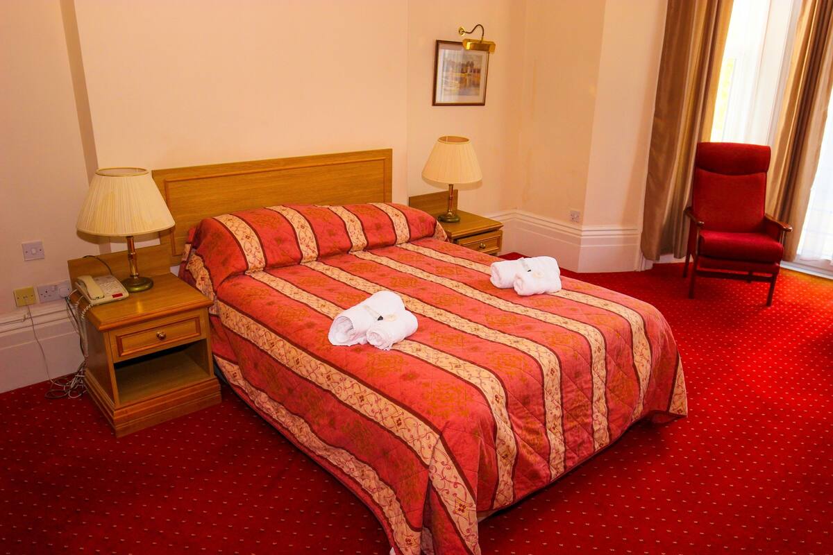 A hotel room with a large bed, two bedside tables with lamps, a red chair, and a red carpet.