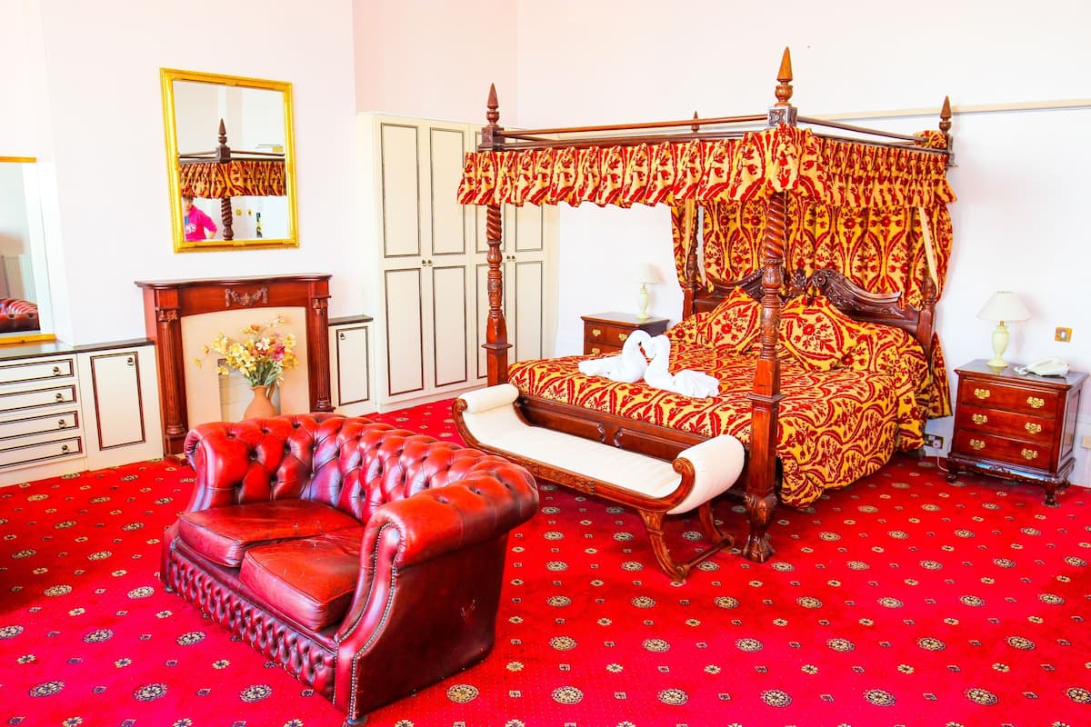 A four-poster bed with a canopy, a red leather sofa, and a red carpeted floor.