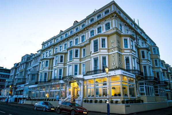 A corner building with multiple stories, featuring a prominent hotel named "Mansion (Lions) Hotel" with a classic architectural style. - The Mansion Lions Hotel (Eastbourne)