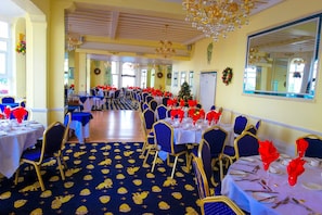 A banquet hall with round tables, blue and gold chairs, and a patterned carpet. - The Mansion Lions Hotel (Eastbourne)