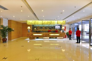 A hotel reception area with a marble counter, a television, and two staff members in red uniforms. - Sunon Hotel (Shenzhen)