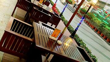 Outdoor wooden tables and chairs arranged on a wooden deck with potted plants and hanging decorations.