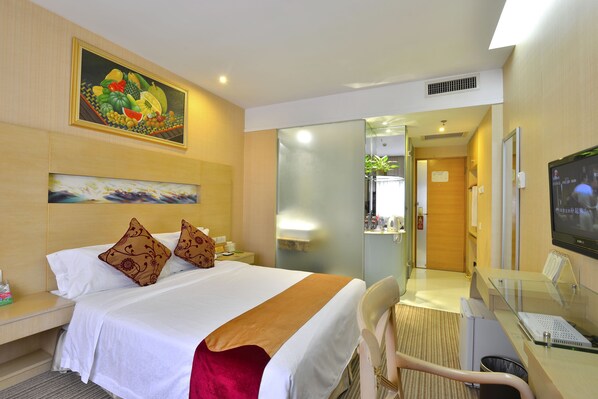 A hotel room with a bed, a desk with a computer, a TV, and a bathroom visible through a glass door. - Sunon Hotel (Shenzhen)
