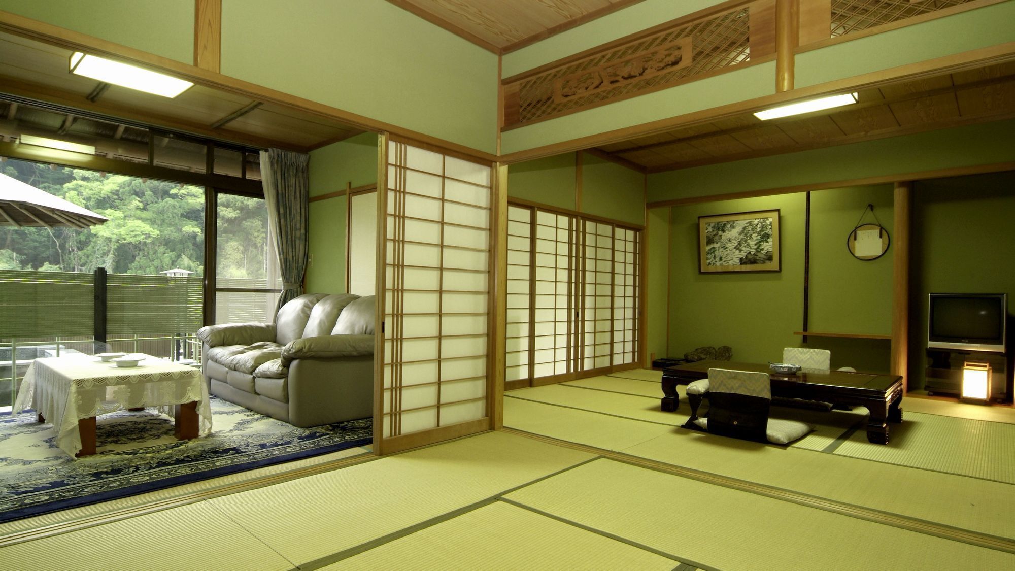 A traditional Japanese room with tatami flooring, a sofa, a low table, a TV, and a sliding door.