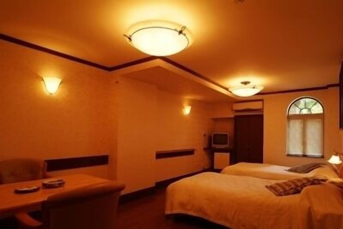 A hotel room with two beds, a desk, a chair, a television, and a window.