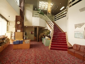 A spacious interior with a red carpeted staircase, a reception desk, and a leather sofa. - Ootaki Hotel (Yugawara)