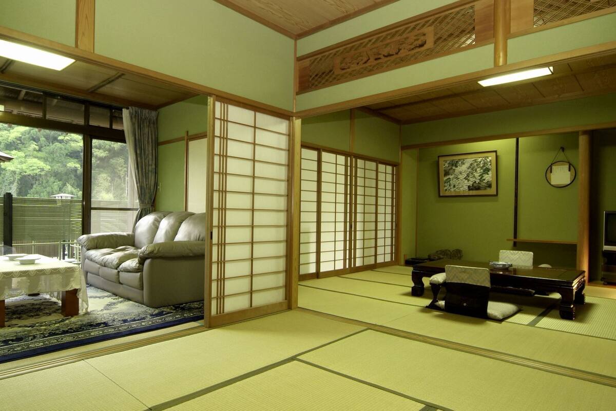 A traditional Japanese room with tatami flooring, a sofa, a table with a cushion, a TV, and a painting on the wall.