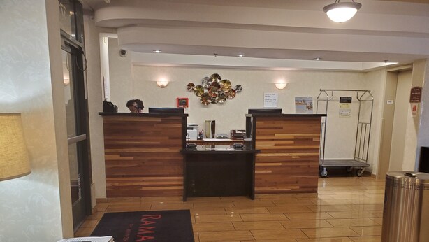 Una zona de recepción con mostradores de madera, un mostrador de registro, un aplique de pared y un carrito metálico.