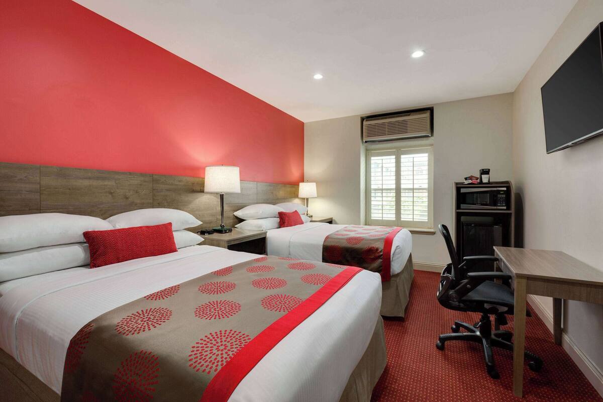 A hotel room with two beds, a desk, a chair, and a TV.