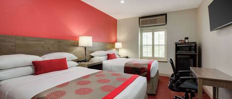 A hotel room with two beds, a desk, a chair, and a TV.