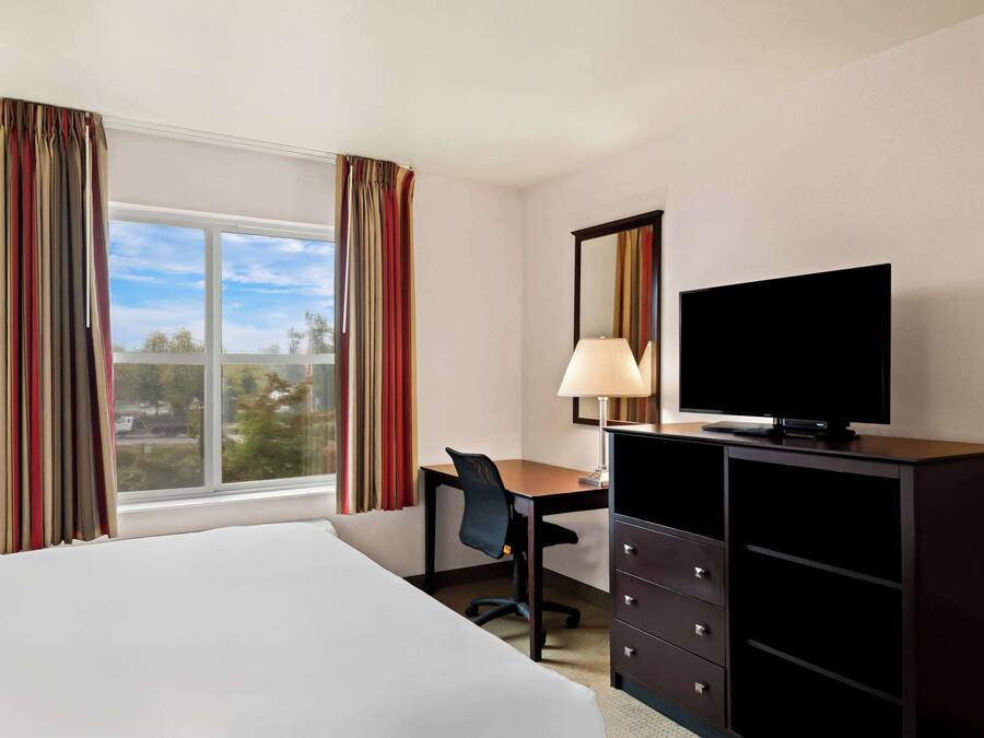A hotel room with a bed, a desk with a chair, a television, and a dresser.