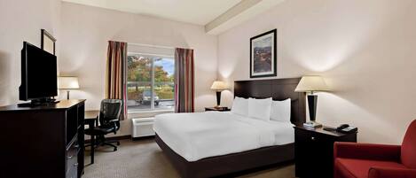 A hotel room with a large bed, a desk with a computer, a TV, a chair, and a red armchair.