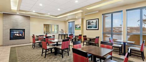 Un espace de restauration dans un hôtel, avec des tables et des chaises, une cheminée et de grandes fenêtres.