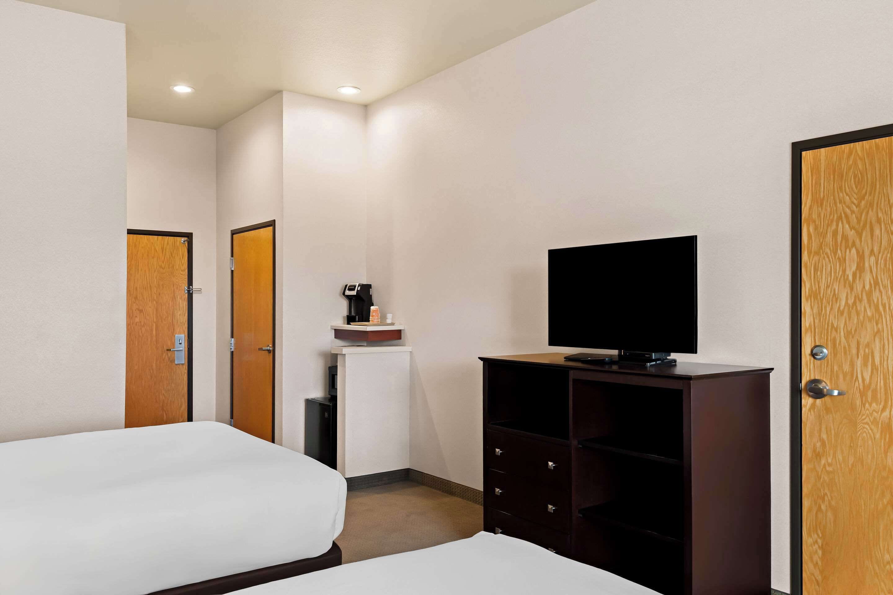 A hotel room with two beds, a TV, a small kitchenette, and a wooden wardrobe.