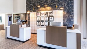 A reception area with two white reception desks, a wall-mounted display with framed artwork, and a modern design with a textured wall and recessed lighting. - Garner Hotel Doswell Southeast by IHG (Doswell)