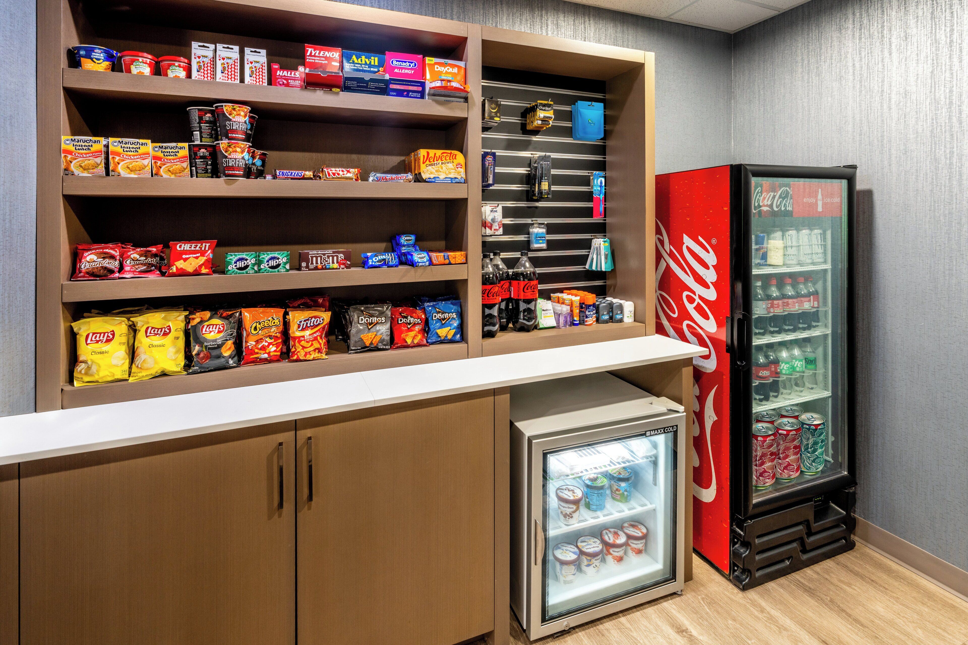A snack and beverage display area with shelves stocked with various snacks and a Coca-Cola refrigerator.