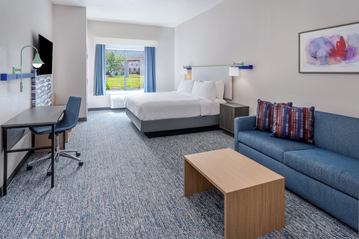 Une chambre d’hôtel avec un lit, un bureau, un canapé bleu et une table basse.