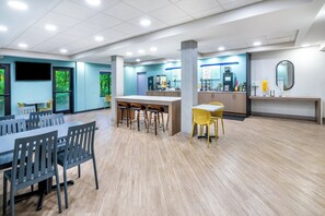 A spacious indoor area with a long table and chairs, a counter with a coffee machine, and a large mirror on the wall. - Garner Hotel Doswell Southeast by IHG (Doswell)