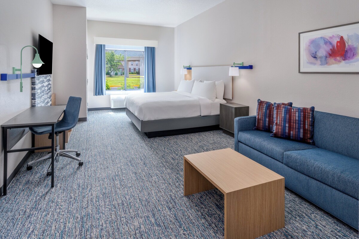 Ein Hotelzimmer mit Bett, Schreibtisch, blauem Sofa und Couchtisch.
