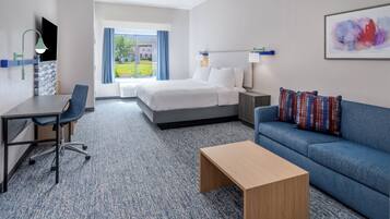 Una habitación de hotel con cama, escritorio, sofá azul y una mesa de centro.