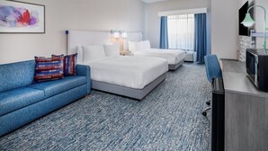 A hotel room with a blue sofa, two beds, a desk, a TV, and a painting on the wall. - Garner Hotel Doswell Southeast by IHG (Doswell)