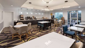 A modern hotel lobby with a central dining area, a kitchen, and large windows offering views.