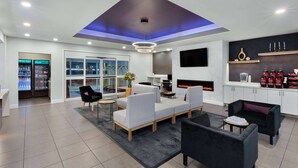 A modern living room with a sofa, chairs, a fireplace, a TV, and a kitchen area with a fridge and shelves.