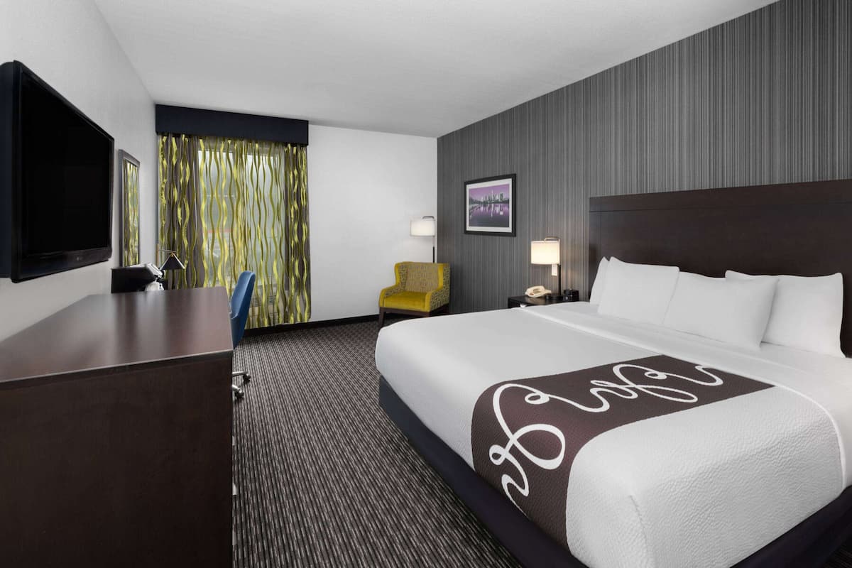 Una habitación de hotel con una cama grande, un escritorio, un televisor, una silla y una ventana con cortinas.