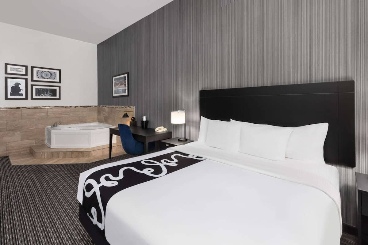 Habitación de hotel con una cama grande, una bañera, un escritorio con lámpara y cuadros en la pared.