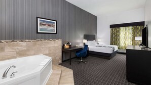 A modern hotel room with a large bathtub, a desk with a chair, a bed, and a television.
