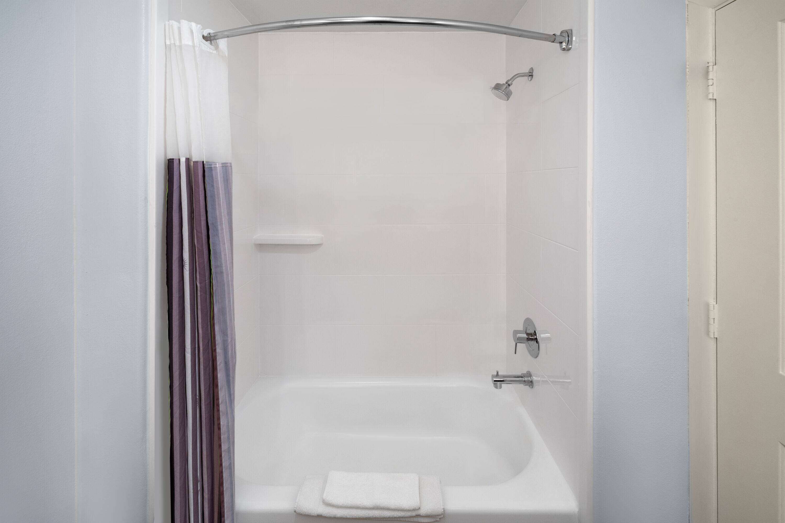 Una ducha moderna con puerta de cristal, una bañera blanca y un cortinón.