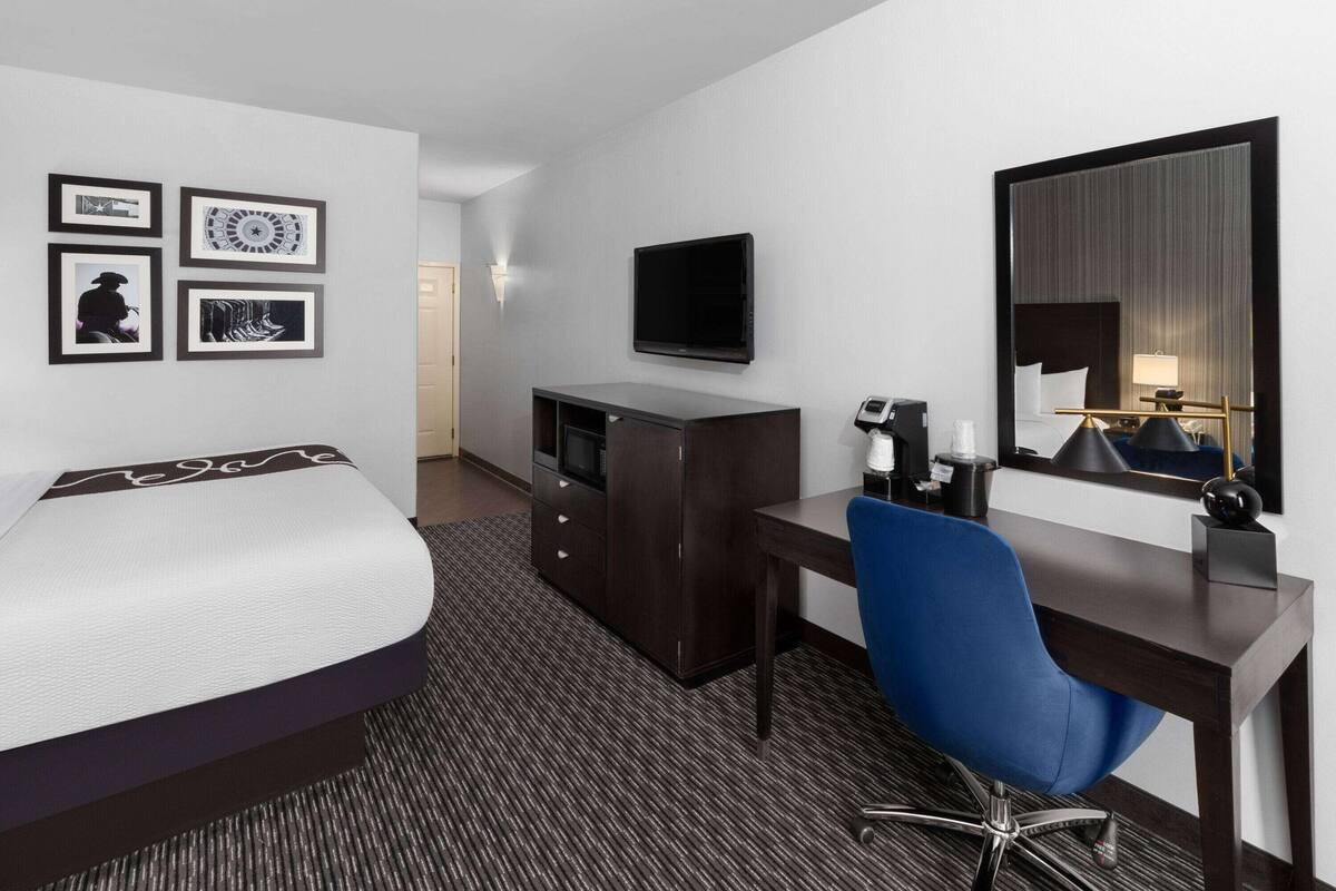 Una habitación de hotel con una cama, un escritorio, una silla, un aparador, un televisor de pantalla plana y obras de arte enmarcadas en la pared.