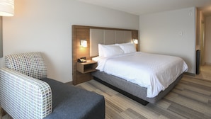 A hotel room with a bed, a chair, a nightstand with a lamp, and a door. - Holiday Inn Express Hotel & Suites Richwood-Cincinnati South by IHG (Walton)