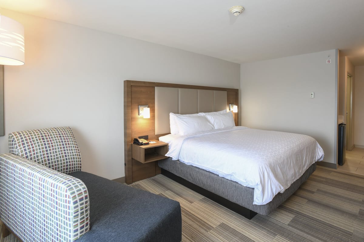 Une chambre d’hôtel avec un lit, une chaise, une table de chevet avec une lampe et une porte.