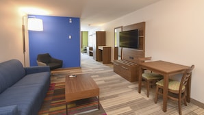 A modern living room with a blue accent wall, a sofa, a coffee table, a TV, and a dining area with chairs. - Holiday Inn Express Hotel & Suites Richwood-Cincinnati South by IHG (Walton)