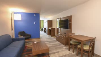 Una sala de estar moderna con una pared azul destacada, un sofá, una mesa de centro, un televisor y un comedor con sillas.