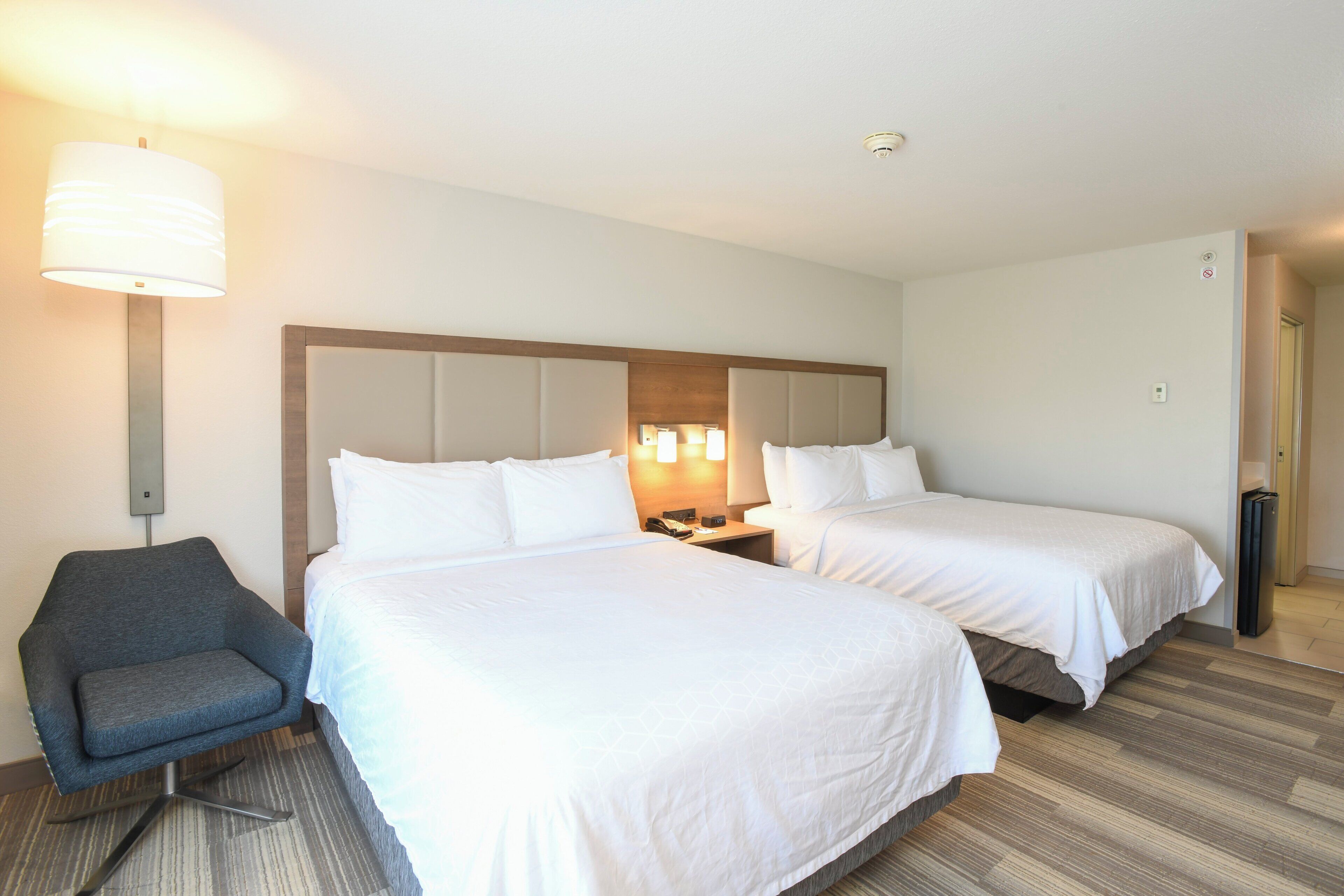 A hotel room with two beds, a chair, a nightstand, and a lamp.