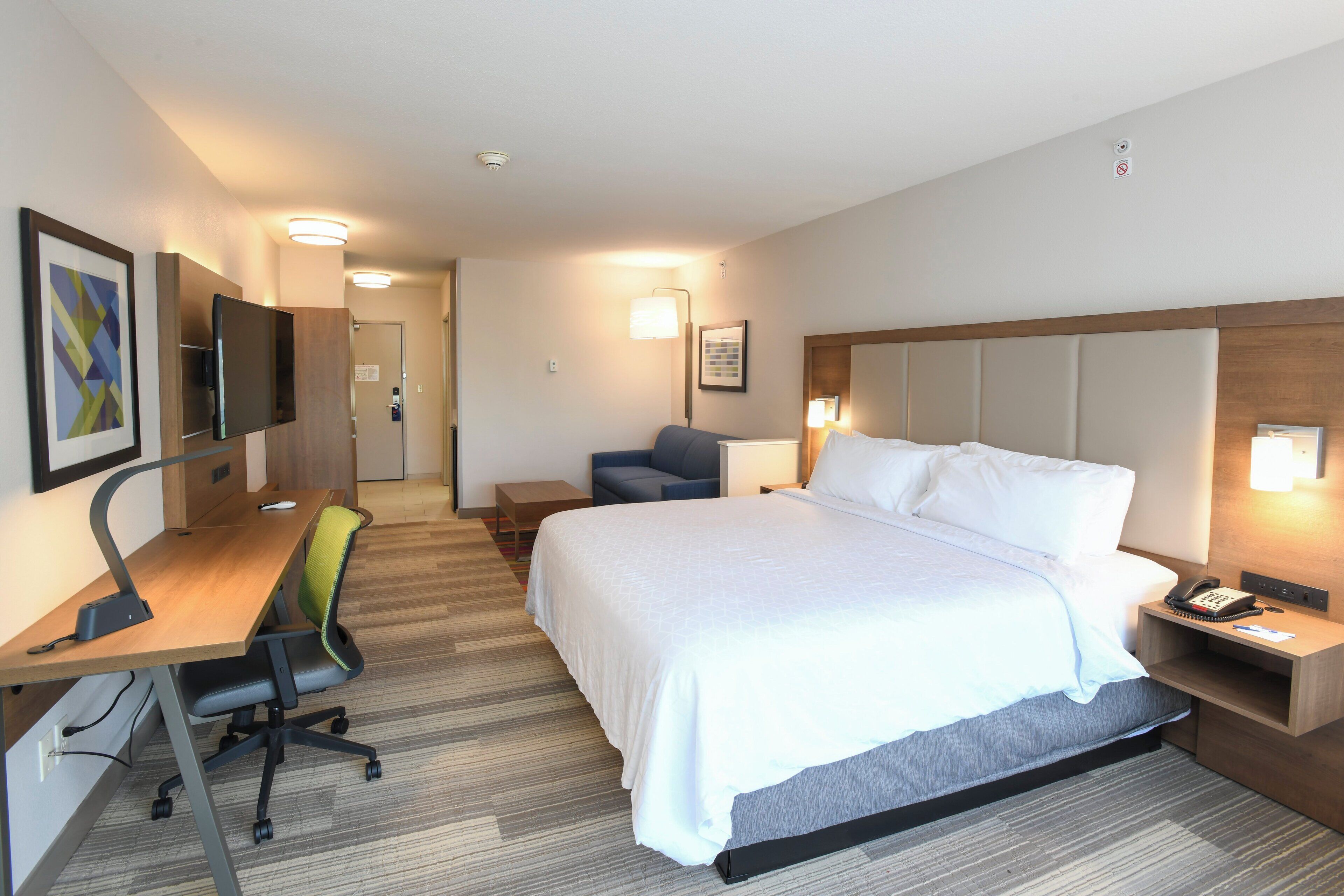 Ett hotellrum med en säng, ett skrivbord, en stol och ett nattduksbord med en telefon.