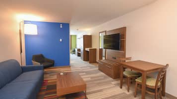 Habitación de hotel moderna con una pared azul de acento, un sofá, un escritorio de madera, un televisor y una alfombra colorida a rayas.