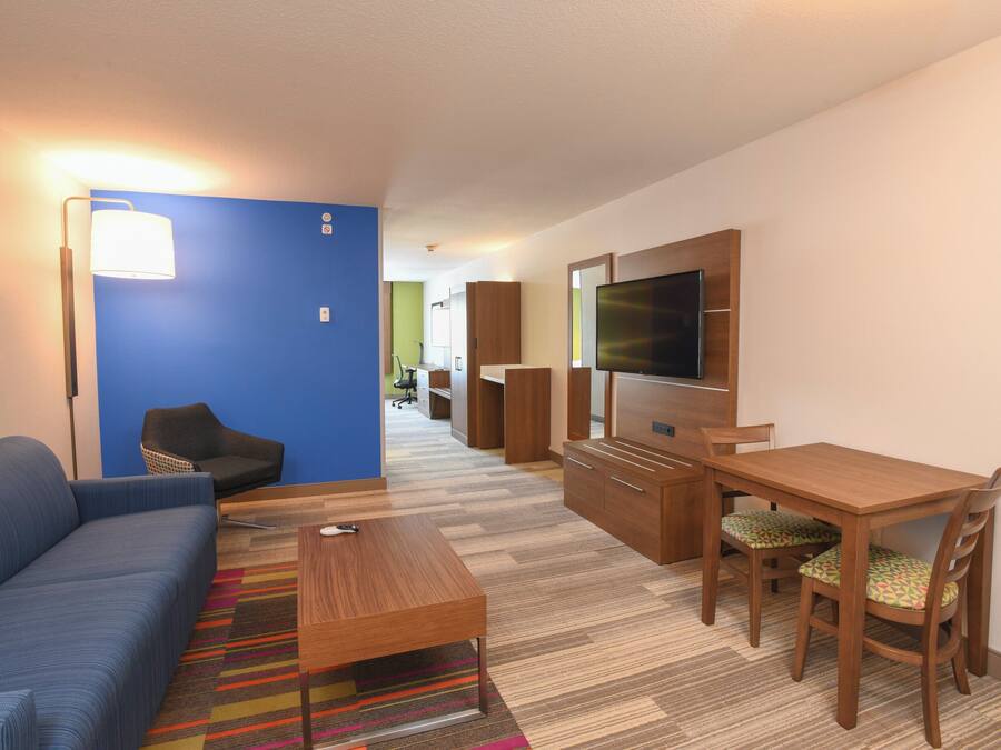 Habitación de hotel moderna con una pared azul de acento, un sofá, un escritorio de madera, un televisor y una alfombra colorida a rayas.